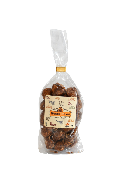 Una bolsa de plástico transparente de 1kg de Nueces De Macadamia Garrapiñadas de Menges de Deus - Alicante, etiquetada "Vegan", "Gluten-Free" y "Monjas en Dulzura", muestra información nutricional y valor energético, sellada con un lazo de oro.
