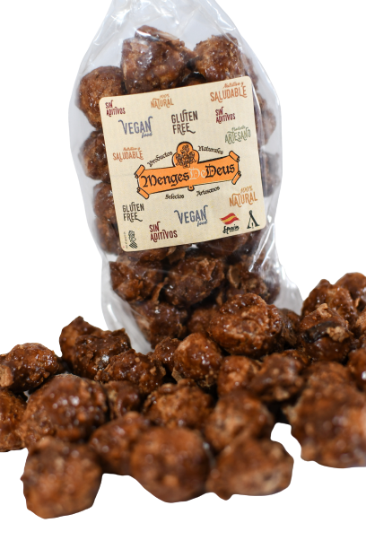 Una bolsa transparente con la etiqueta "Menges de Deus - Alicante - Cerdá, 104. 03009 Alicante" contiene Nueces De Macadamia Garrapiñadas veganas y sin gluten de color marrón y forma irregular de 1kg, con algunos bocadillos derramados por delante.