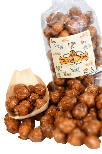Una bolsa de 1kg de Avellanas Garrapiñadas de Menges de Deus, etiquetadas sin gluten y veganas con información nutricional en el envase, más algunas avellanas en un cacito de madera y esparcidas. Marca: Alicante - Cerdá, 104. 03009 Alicante.