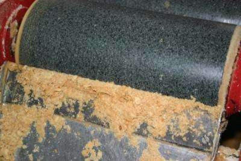 Primer plano de una máquina para trabajar la madera con tambor lijador y serrín sobre metal debajo, texturas que recuerdan la elaboración artesanal del Turrón a la Piedra Artesano El Abuelo (Jijona S.A., caja de madera de 300 g).