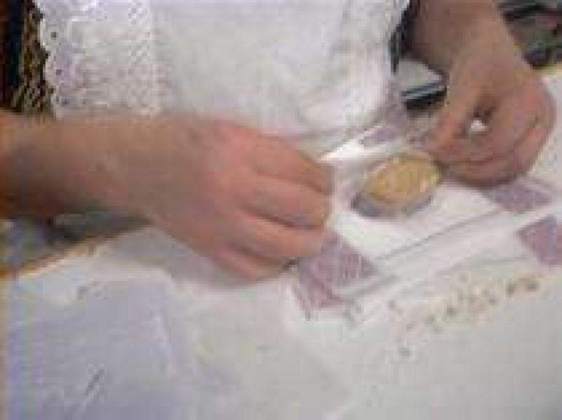 Una persona vestida de blanco envuelve un Polvorón de Almendra sin azúcares añadidos (Jijona S.A., 500g) en una encimera, con papel y utensilios cerca.